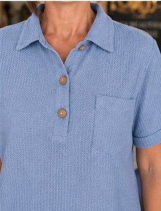 Close-up of a blue textured polo shirt with buttons and a pocket.