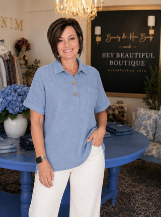 Woman in a blue shirt standing in a boutique with a chandelier and decorative elements.