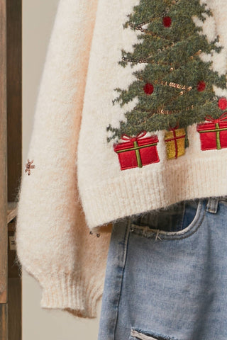Close-up of embroidered Christmas tree and presents on cream cardigan