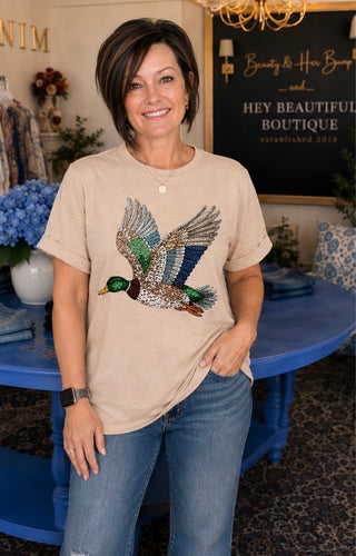 Woman wearing a beige t-shirt with a decorative duck design in a store setting.