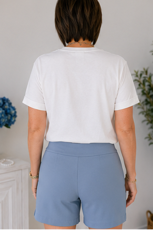 Person wearing a white t-shirt and light blue shorts with a neutral background