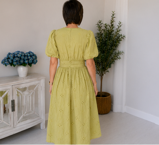 Woman wearing a light green dress standing in a room with a white cabinet and plants.