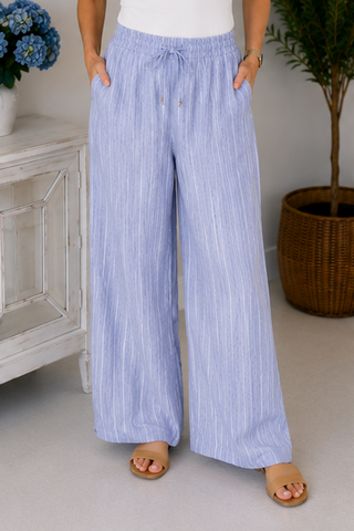Person wearing light blue striped pants in a home setting with a cabinet and plant.