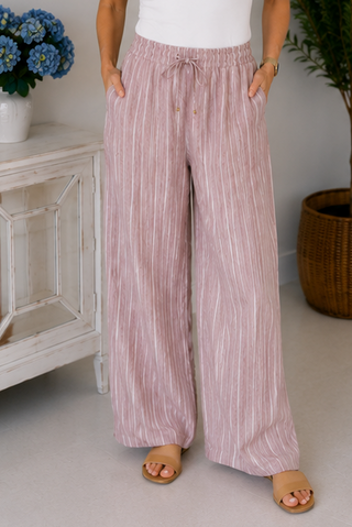Person wearing pink striped pants standing in a room with a white cabinet and plant.