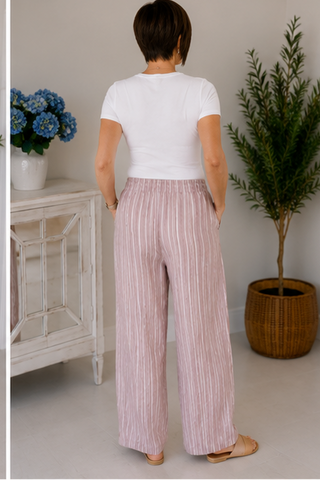 Person wearing a white top and pink striped pants in a room with plants and furniture.