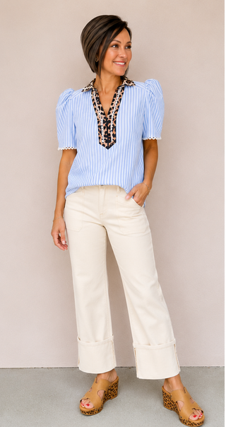 Woman wearing a blue striped blouse with leopard print accents and white pants against a beige background