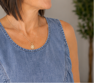 Person wearing a blue sleeveless top with a necklace featuring a pendant.