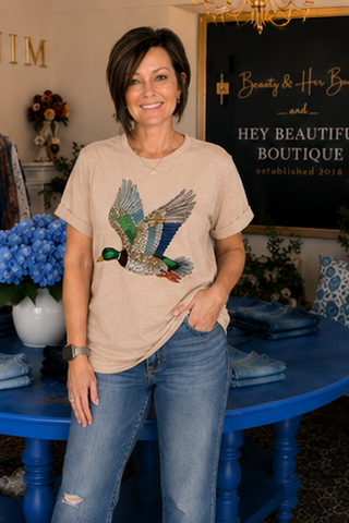 Woman wearing a beige t-shirt with a duck design in a decorated room.