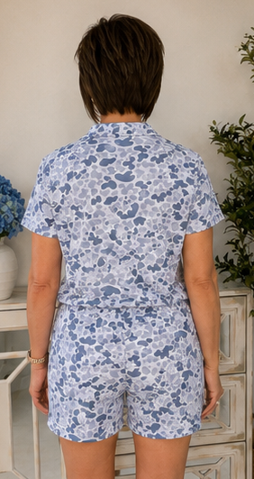 Person wearing a blue floral romper in a room with a white dresser and plant.