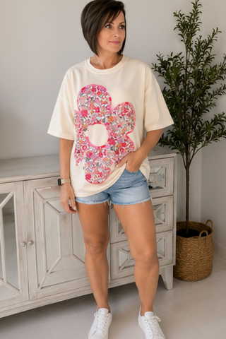 Woman wearing a white t-shirt with a colorful floral design and denim shorts indoors.