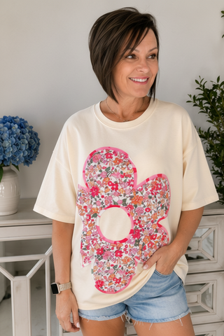 Woman wearing a cream t-shirt with a large floral number 8 design, standing indoors.