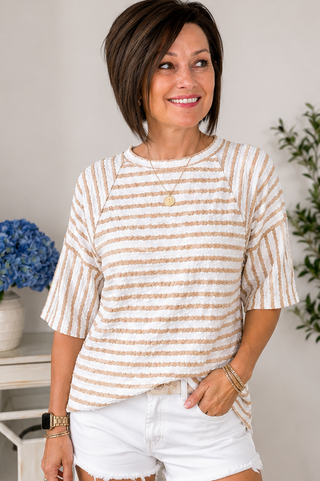 Woman wearing a striped shirt and white shorts indoors with plants in the background