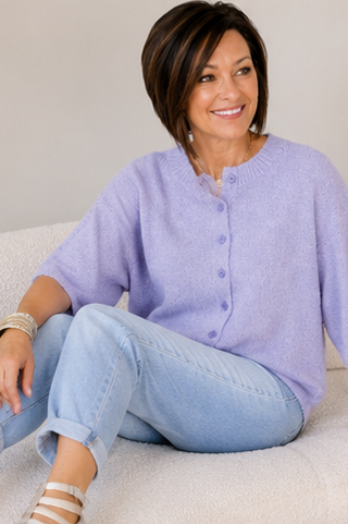 Woman wearing a light purple cardigan and light blue jeans sitting on a couch.