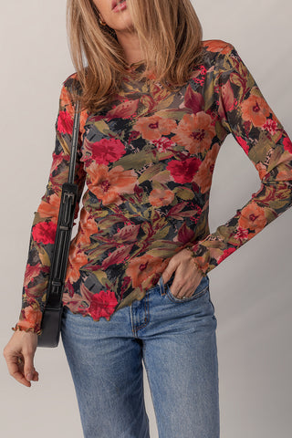 Woman wearing rust and crimson floral mesh long sleeve top with light wash jeans and black crossbody bag