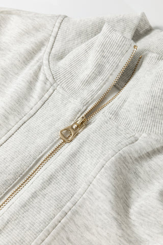 Close-up of a gray zip-up hoodie with a gold zipper on a light gray background