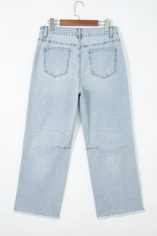 Light blue jeans hanging on a wooden hanger against a white background