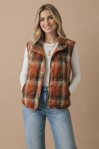Rust plaid quilted puffer vest with high neck and snap front over a cream long sleeve top